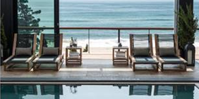 A pool with chairs and tables in front of the ocean.